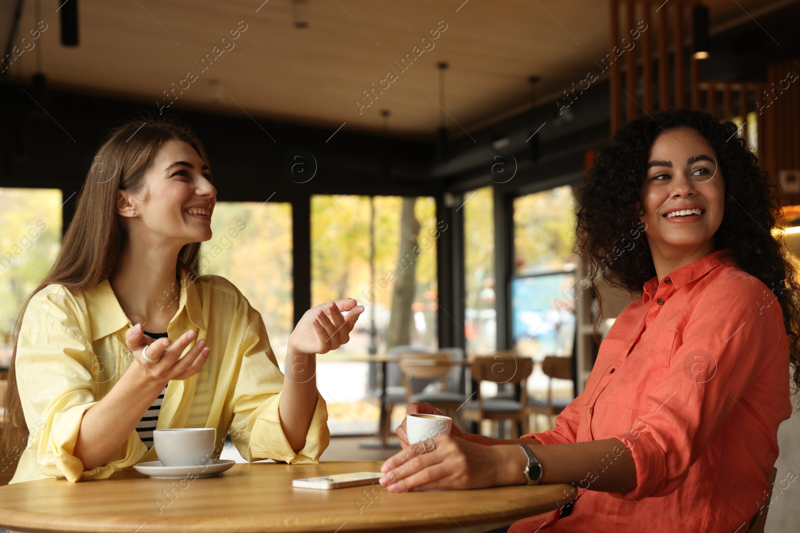 Photo of Happy women with coffee drinks chatting in cafe