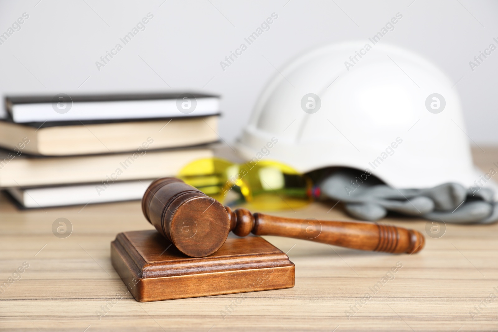 Photo of Accident at work concept. Gavel, books and construction worker's protective gear on wooden table, selective focus