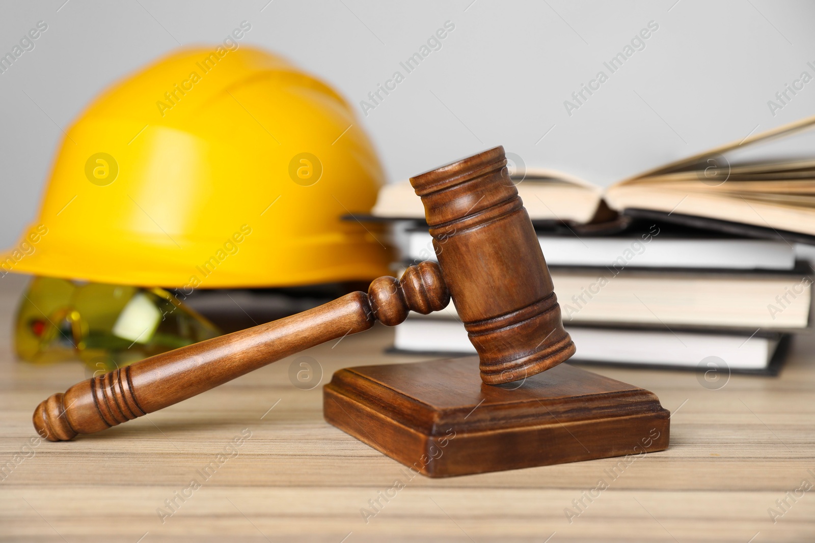 Photo of Accident at work concept. Gavel, books and construction worker's protective gear on wooden table, selective focus