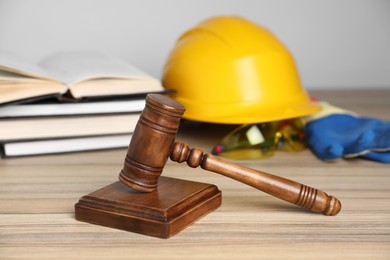 Photo of Accident at work concept. Gavel, books and construction worker's protective gear on wooden table, selective focus