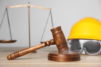 Photo of Accident at work concept. Gavel, scales and construction worker's protective gear on wooden table, selective focus