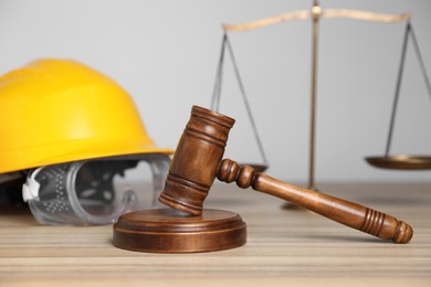 Photo of Accident at work concept. Gavel, scales and construction worker's protective gear on wooden table, selective focus