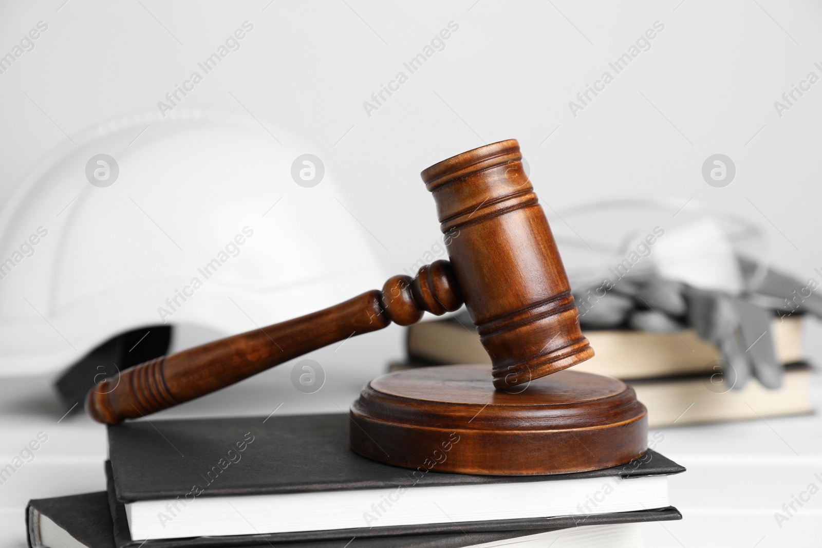 Photo of Accident at work concept. Gavel, books and construction worker's protective gear on white wooden table, selective focus