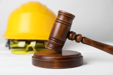 Photo of Accident at work concept. Gavel and construction worker's protective gear on white wooden table, selective focus