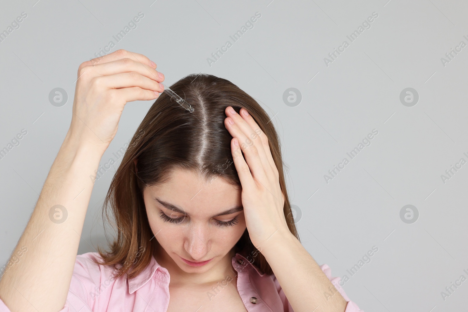 Photo of Hair loss problem. Girl applying serum onto hairline on grey background