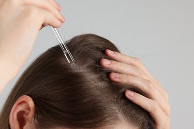 Photo of Hair loss problem. Girl applying serum onto hairline on grey background, closeup