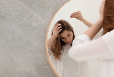 Photo of Hair loss problem. Girl applying serum onto hairline near mirror in bathroom, space for text