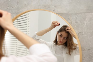 Photo of Hair loss problem. Girl applying serum onto hairline near mirror in bathroom