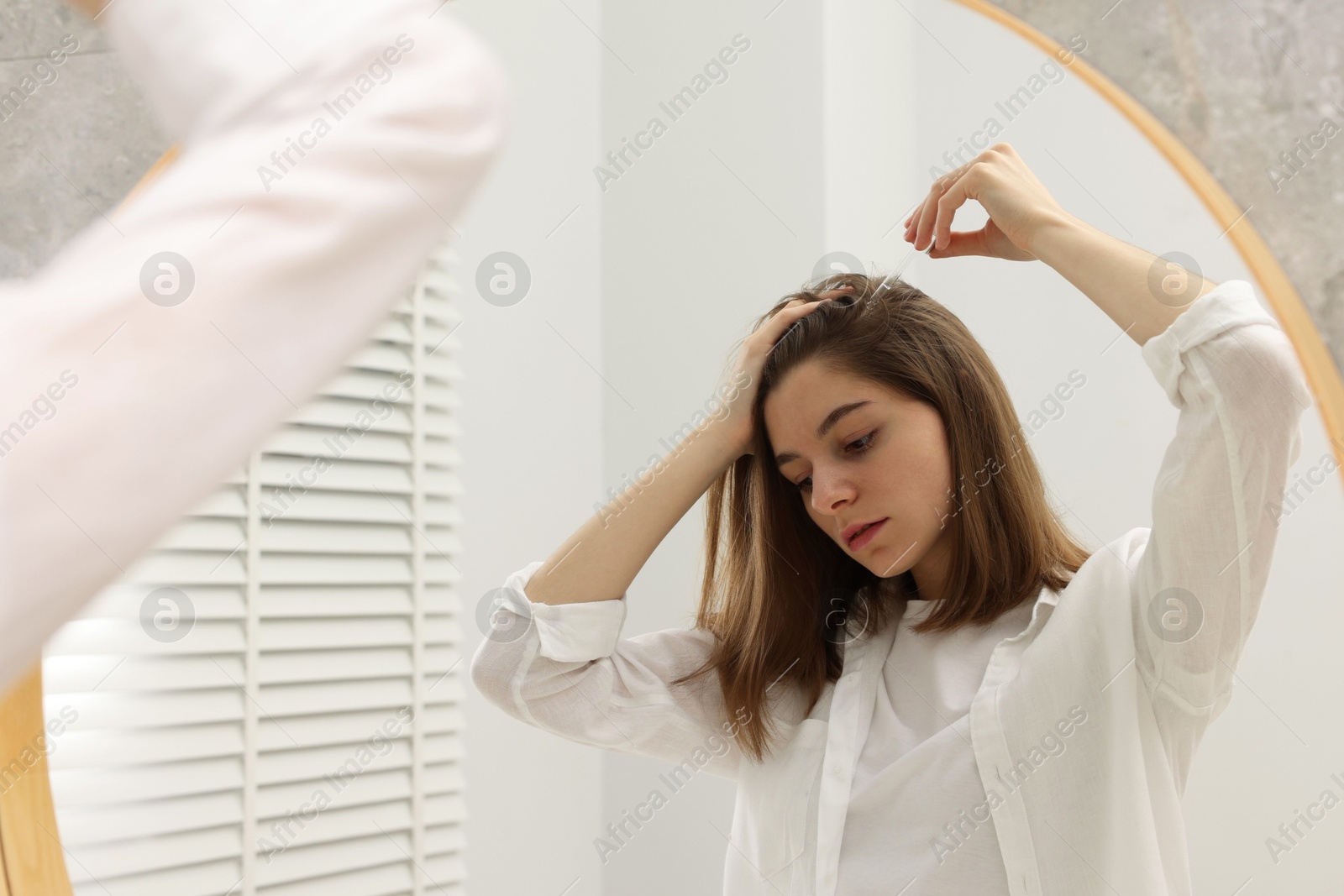 Photo of Hair loss problem. Girl applying serum onto hairline near mirror in bathroom