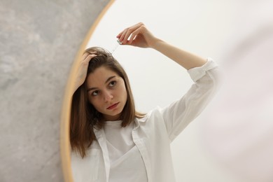 Photo of Hair loss problem. Girl applying serum onto hairline near mirror in bathroom