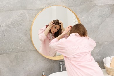 Photo of Girl with hair loss problem near mirror in bathroom