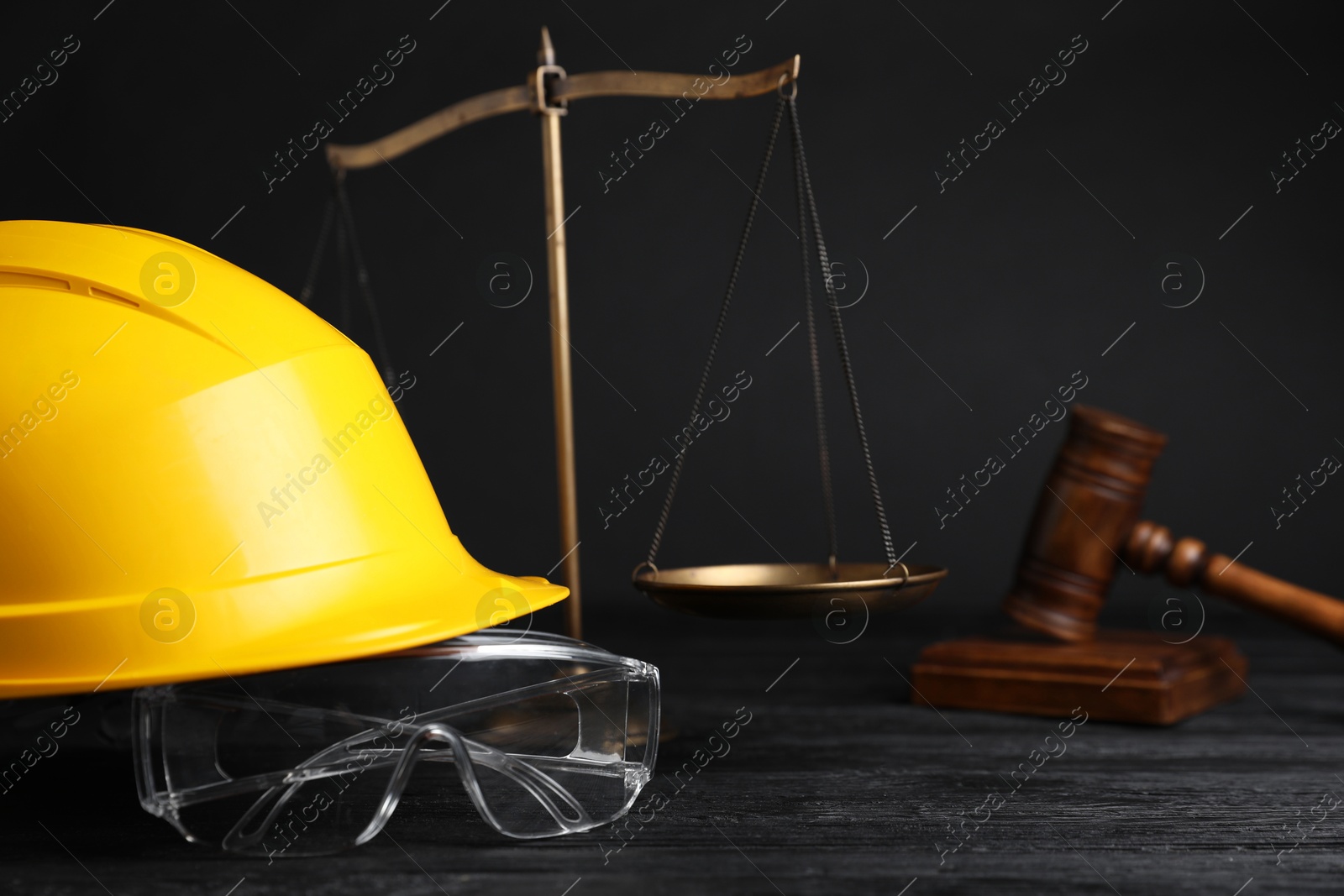 Photo of Accident at work concept. Gavel, scales and construction worker's protective gear on black wooden table, selective focus