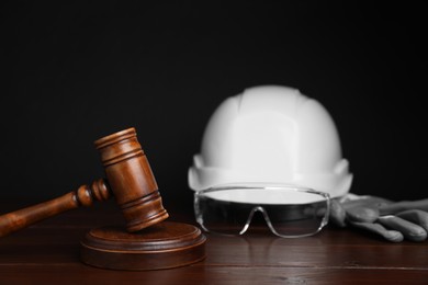 Photo of Accident at work concept. Gavel and construction worker's protective gear on wooden table, selective focus