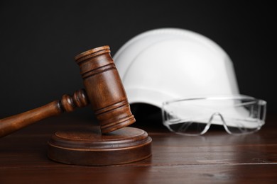 Photo of Accident at work concept. Gavel and construction worker's protective gear on wooden table, selective focus