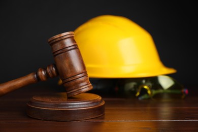 Photo of Accident at work concept. Gavel and construction worker's protective gear on wooden table, selective focus