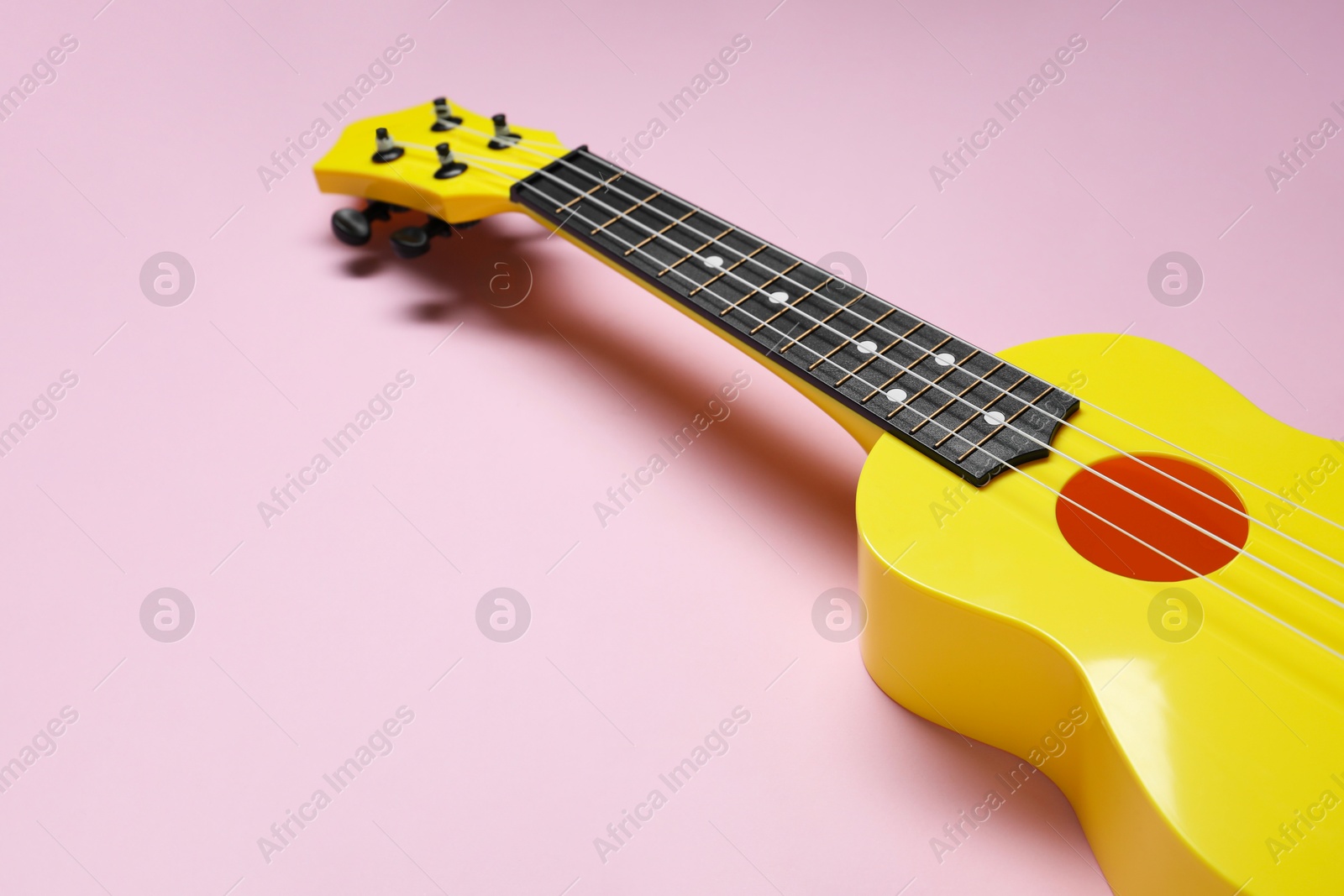 Photo of One ukulele on pink background, closeup. String musical instrument