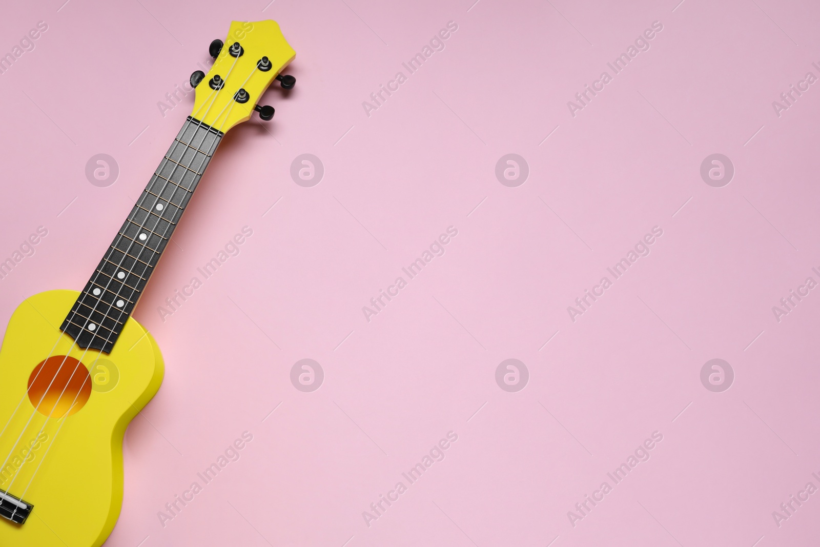 Photo of One ukulele on pink background, top view. Space for text