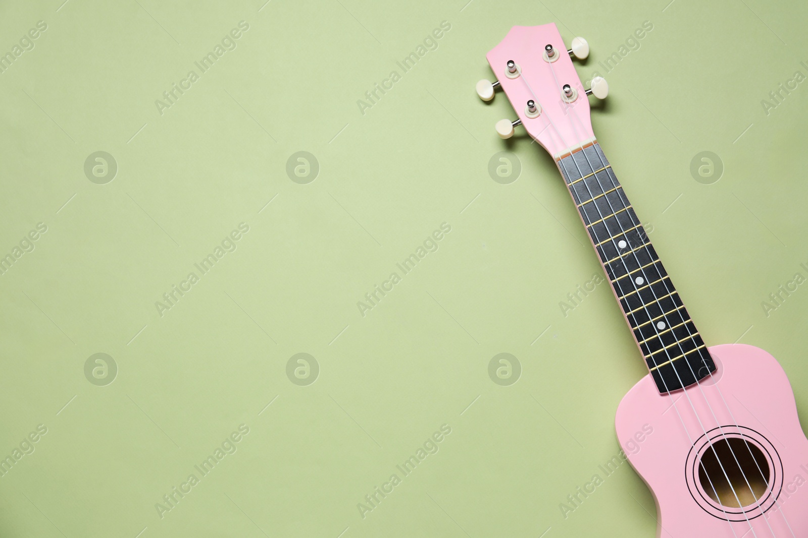 Photo of One ukulele on light olive background, top view. Space for text