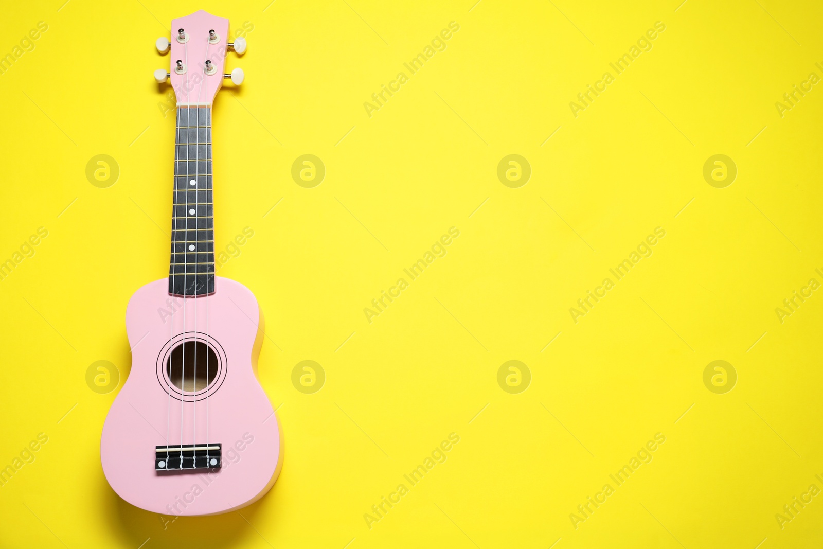 Photo of One ukulele on yellow background, top view. Space for text