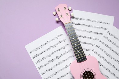 Photo of Ukulele and music sheets on violet background, top view. Space for text