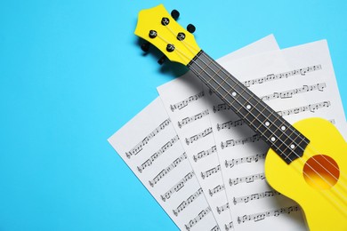 Photo of Ukulele and music sheets on light blue background, top view. Space for text