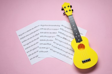 Photo of Ukulele and music sheets on pink background, top view