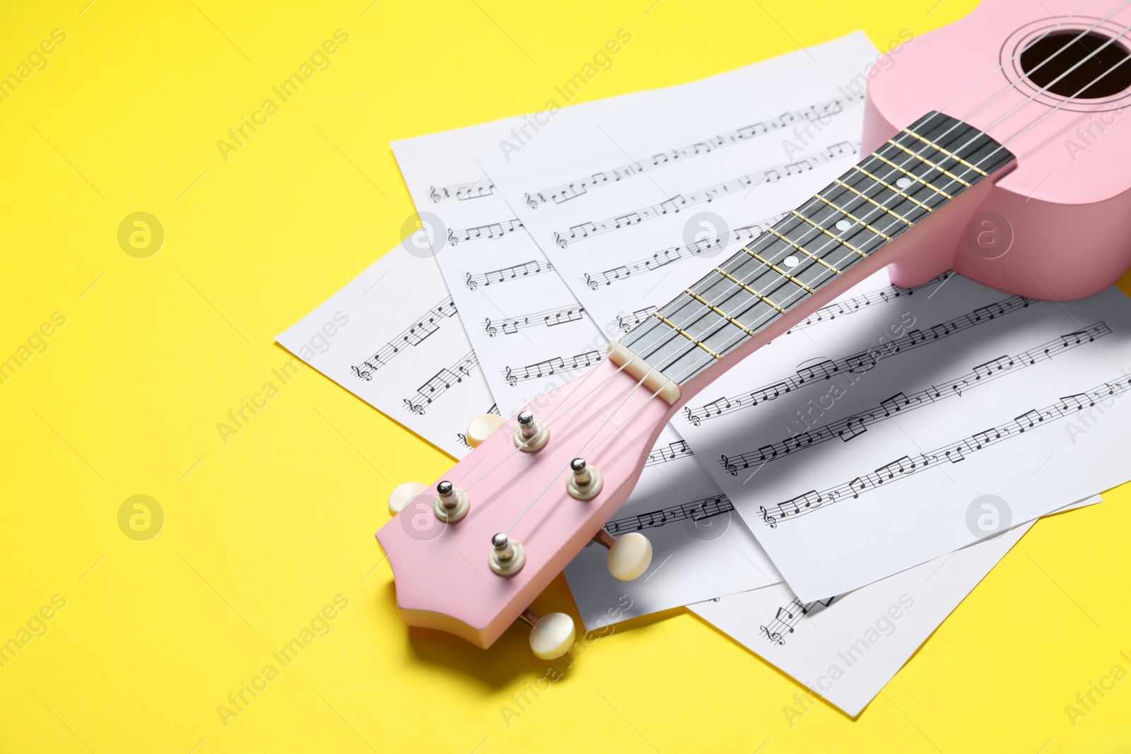 Photo of Ukulele and music sheets on yellow background