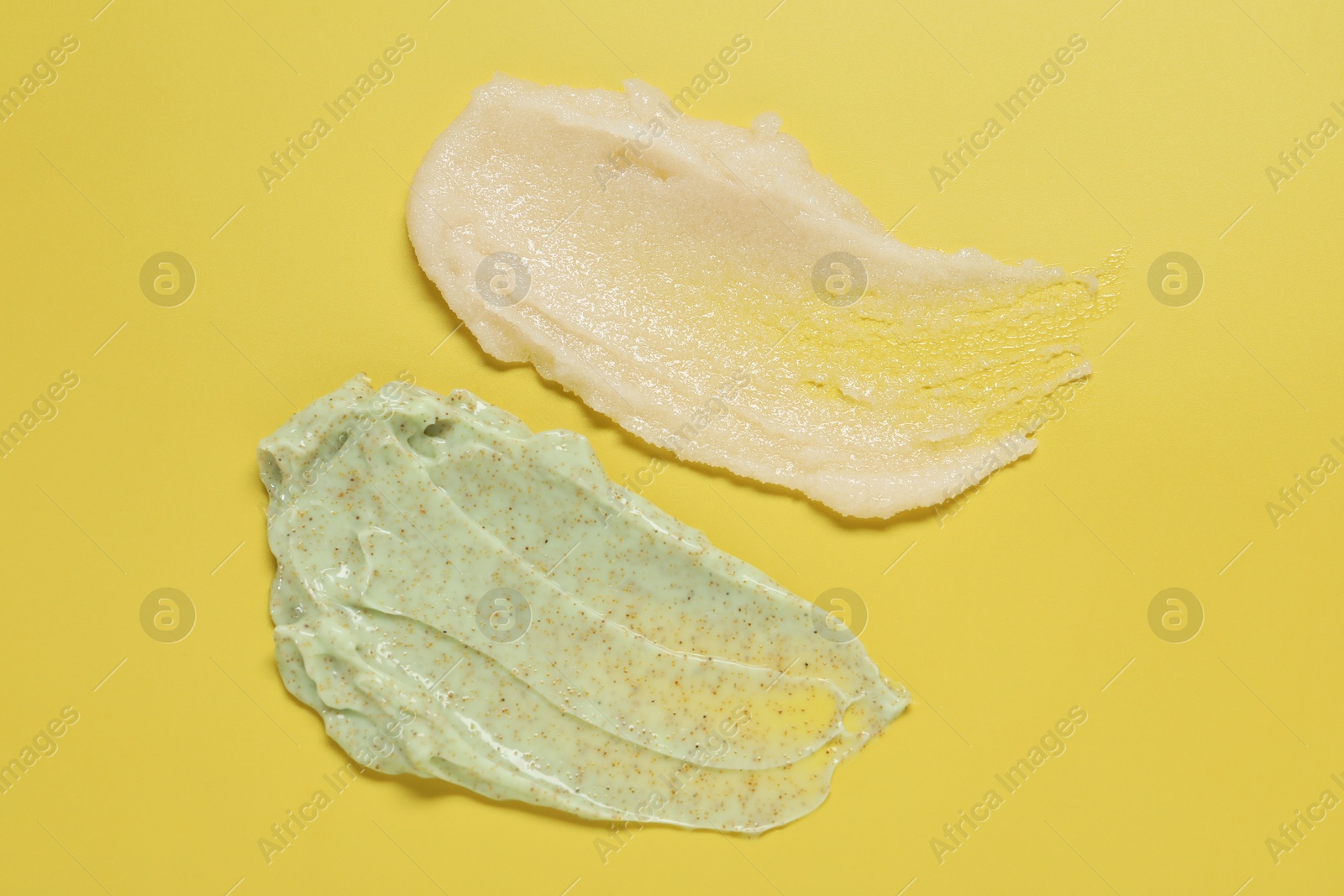 Photo of Samples of different body scrubs on yellow background, top view