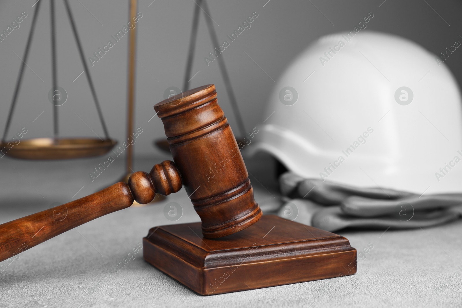 Photo of Accident at work. Gavel, safety equipment and scales on grey textured table, selective focus