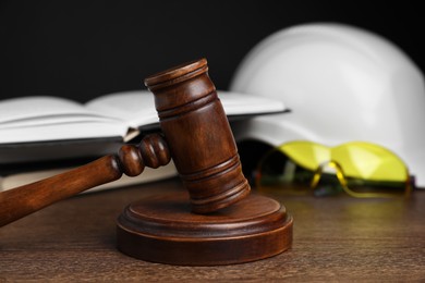 Photo of Accident at work. Gavel, safety equipment and books on wooden table, selective focus