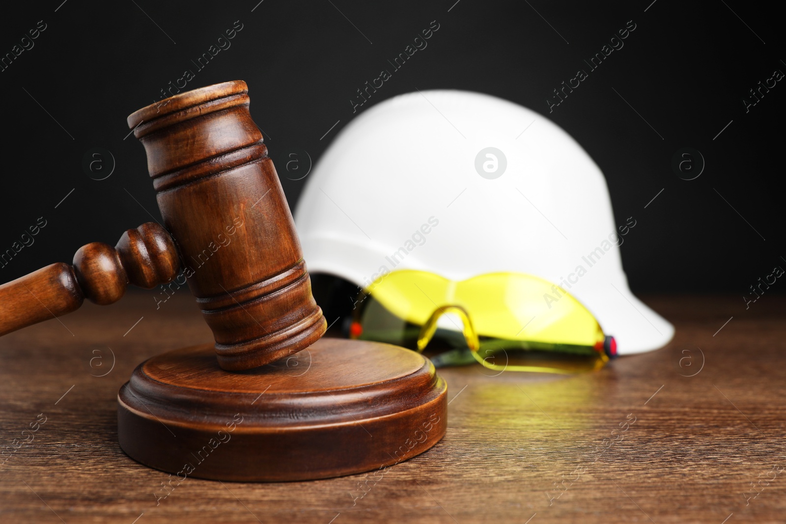 Photo of Accident at work. Gavel, hardhat and goggles on wooden table, selective focus