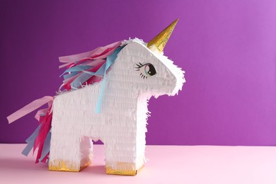 Photo of Bright pinata in shape of unicorn on color background, space for text