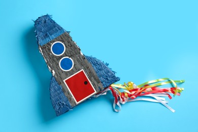 Photo of Bright pinata in shape of spaceship on light blue background, top view