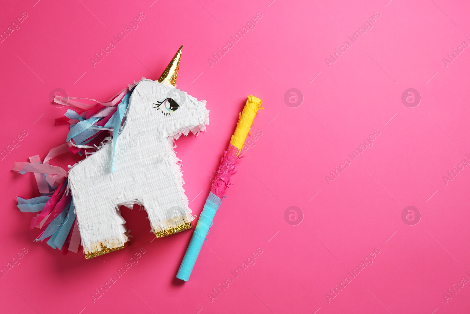 Photo of Bright pinata in shape of unicorn and stick on pink background, top view. Space for text