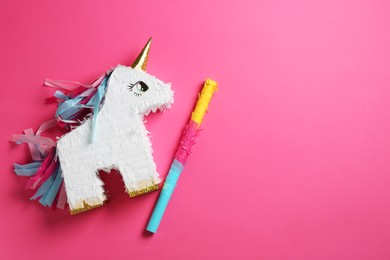 Photo of Bright pinata in shape of unicorn and stick on pink background, top view. Space for text