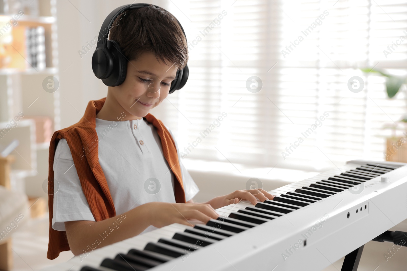 Photo of Cute boy in headphones playing synthesizer at home. Space for text