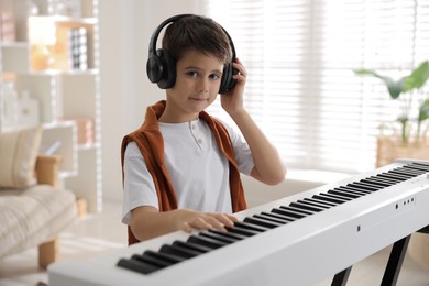 Photo of Cute boy in headphones playing synthesizer at home