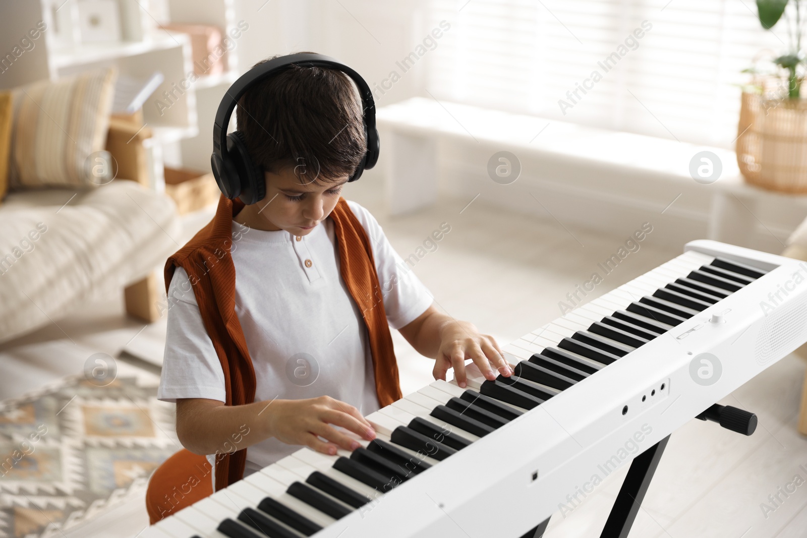 Photo of Cute boy in headphones playing synthesizer at home