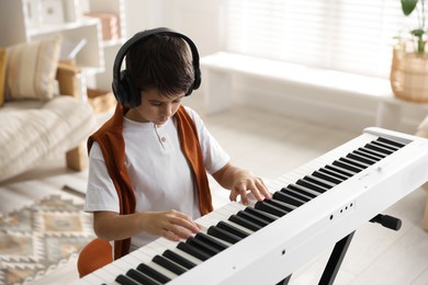 Photo of Cute boy in headphones playing synthesizer at home