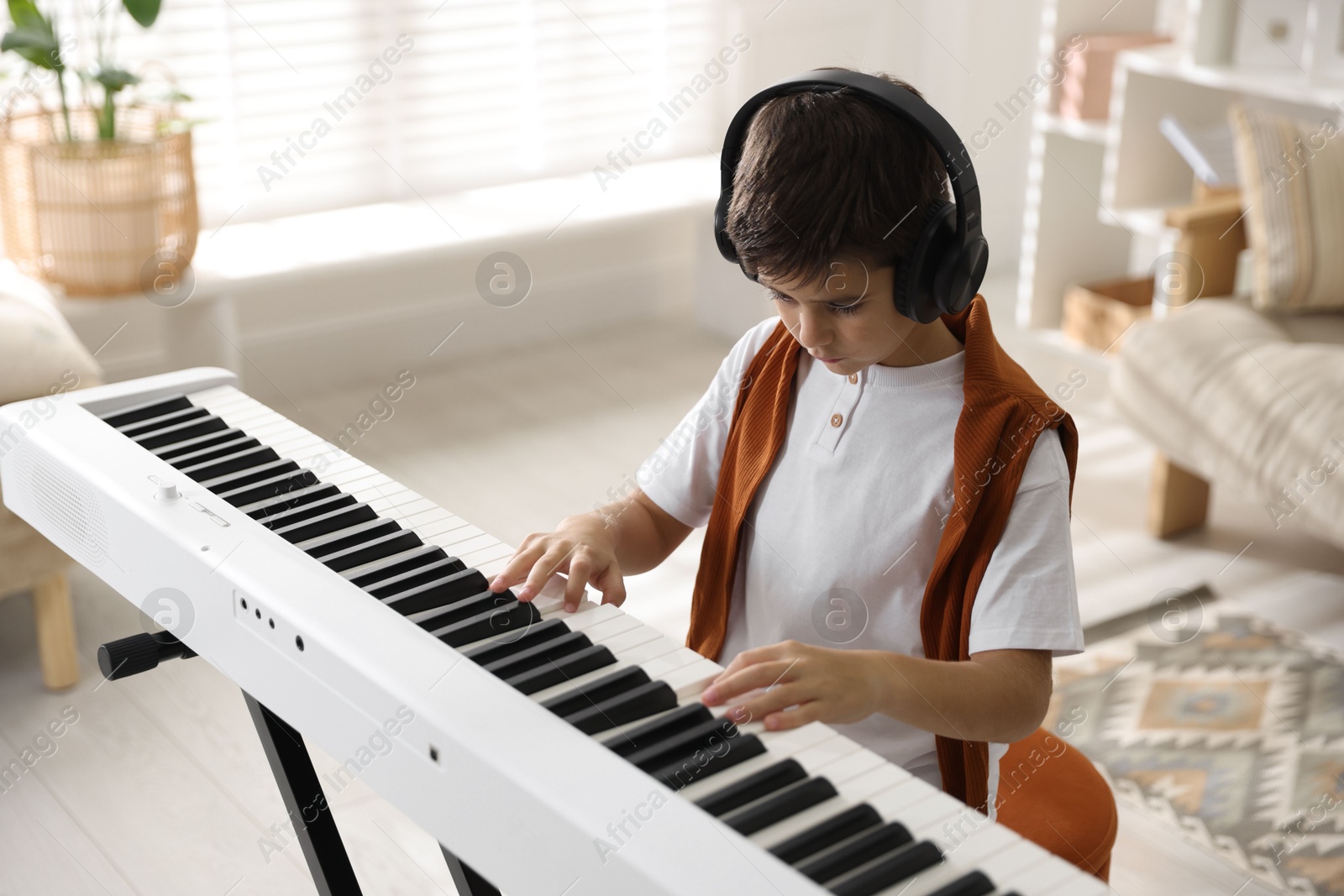 Photo of Cute boy in headphones playing synthesizer at home