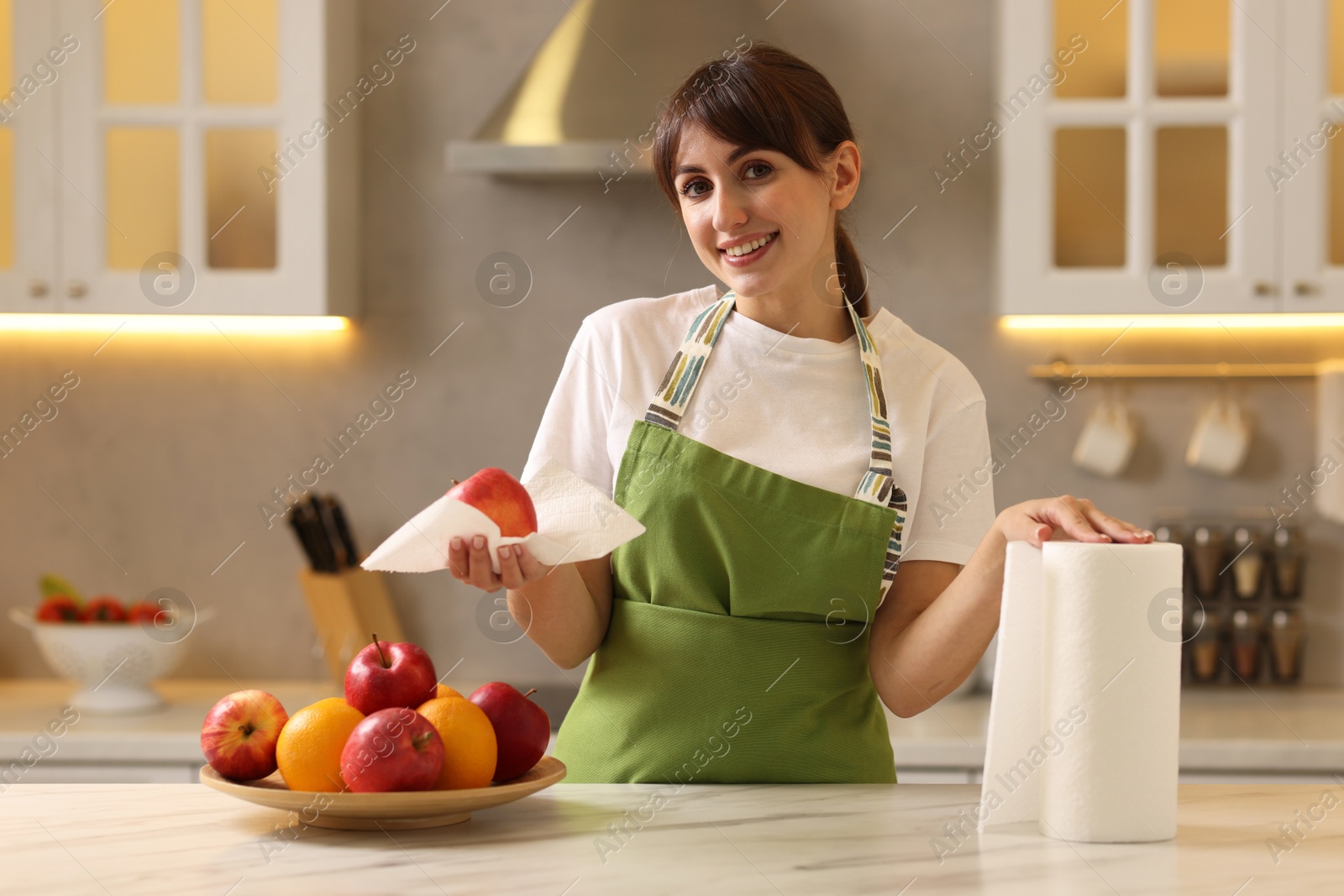 Photo of Woman wiping apple with paper towel at white marble table in kitchen