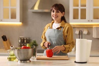 Photo of Woman cutting bell pepper at white marble table with paper towel in kitchen