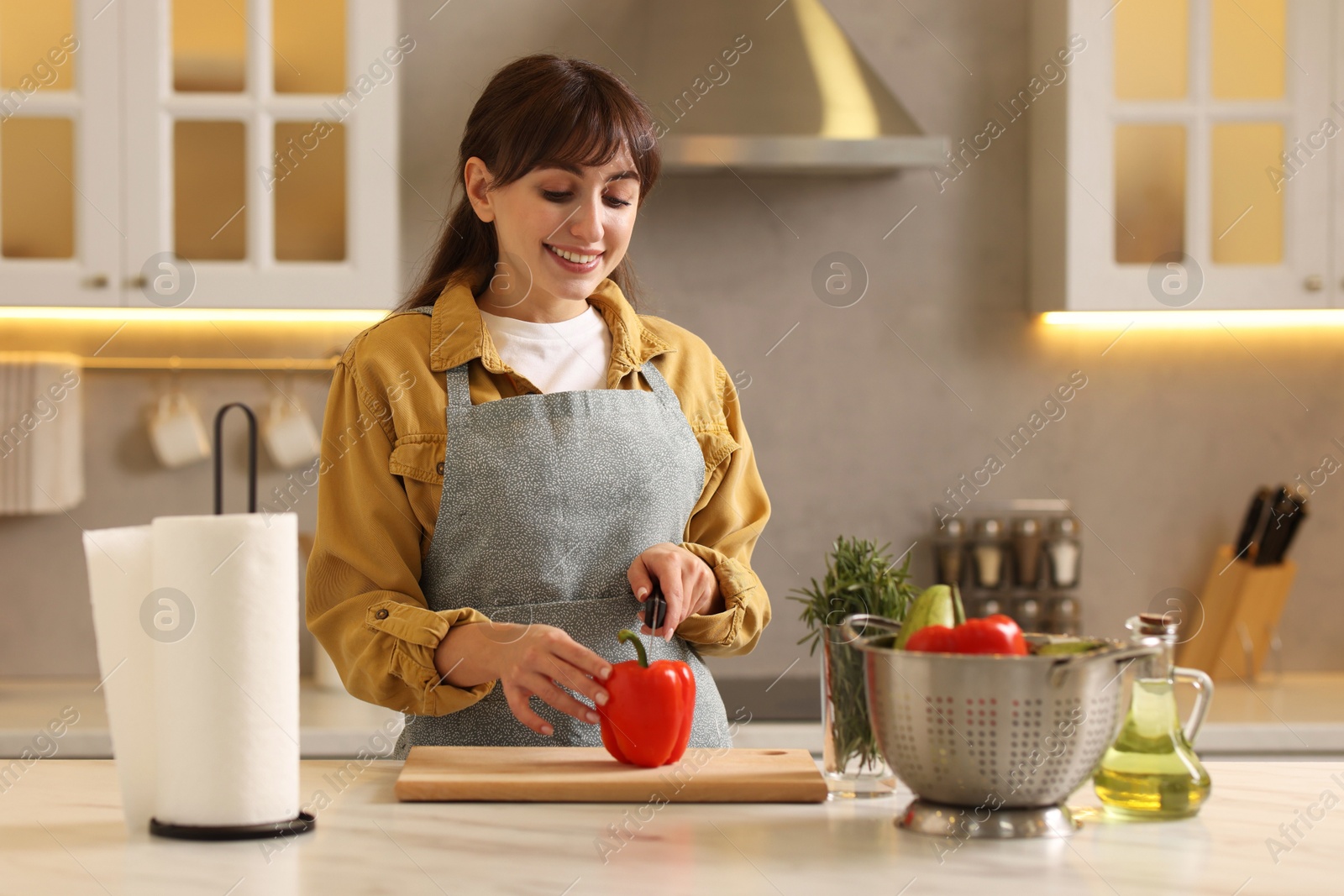 Photo of Woman cutting bell pepper at white marble table with paper towel in kitchen