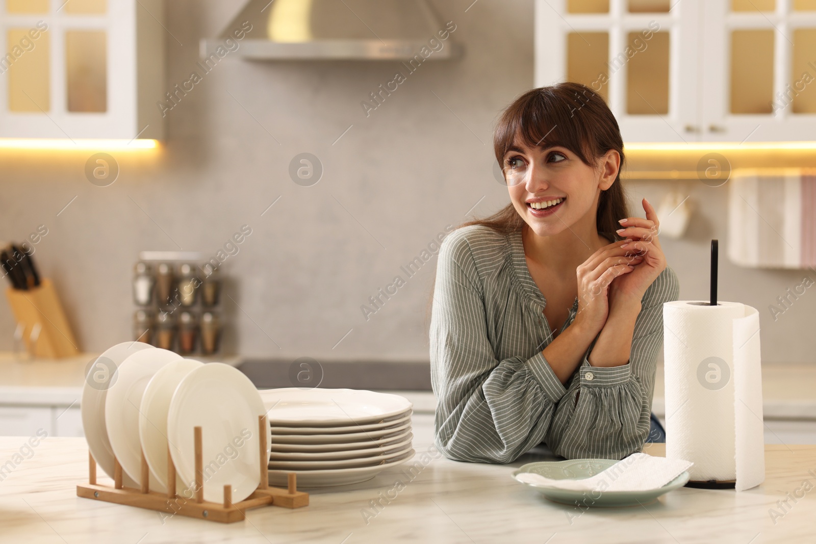 Photo of Woman at white marble table with roll of towels and clean plates in kitchen