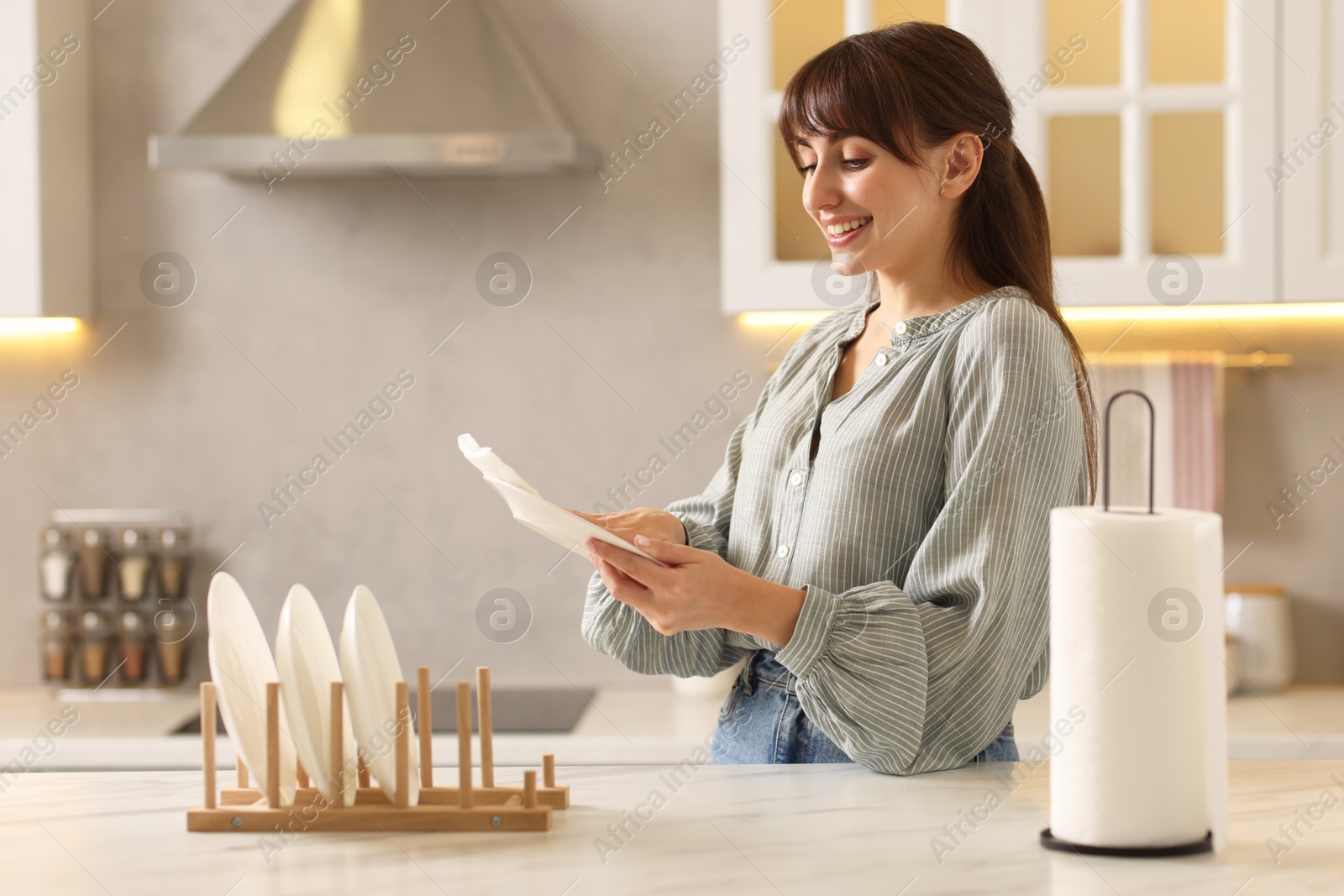 Photo of Woman wiping plate with paper towel at white marble table in kitchen