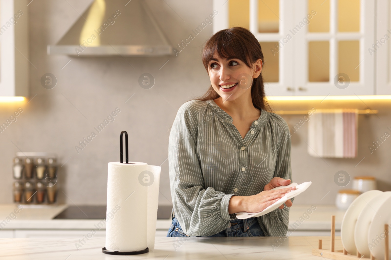 Photo of Woman wiping plate with paper towel at white marble table in kitchen