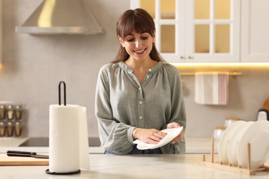 Photo of Woman wiping plate with paper towel at white marble table in kitchen