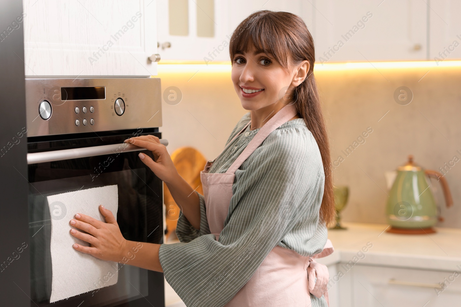 Photo of Smiling woman wiping oven with paper towel in kitchen