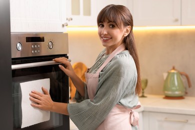 Photo of Smiling woman wiping oven with paper towel in kitchen