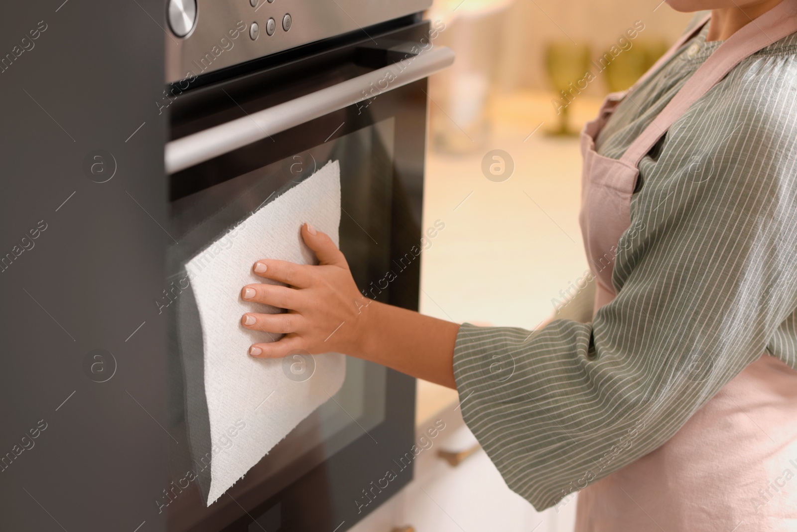 Photo of Woman wiping oven with paper towel in kitchen, closeup